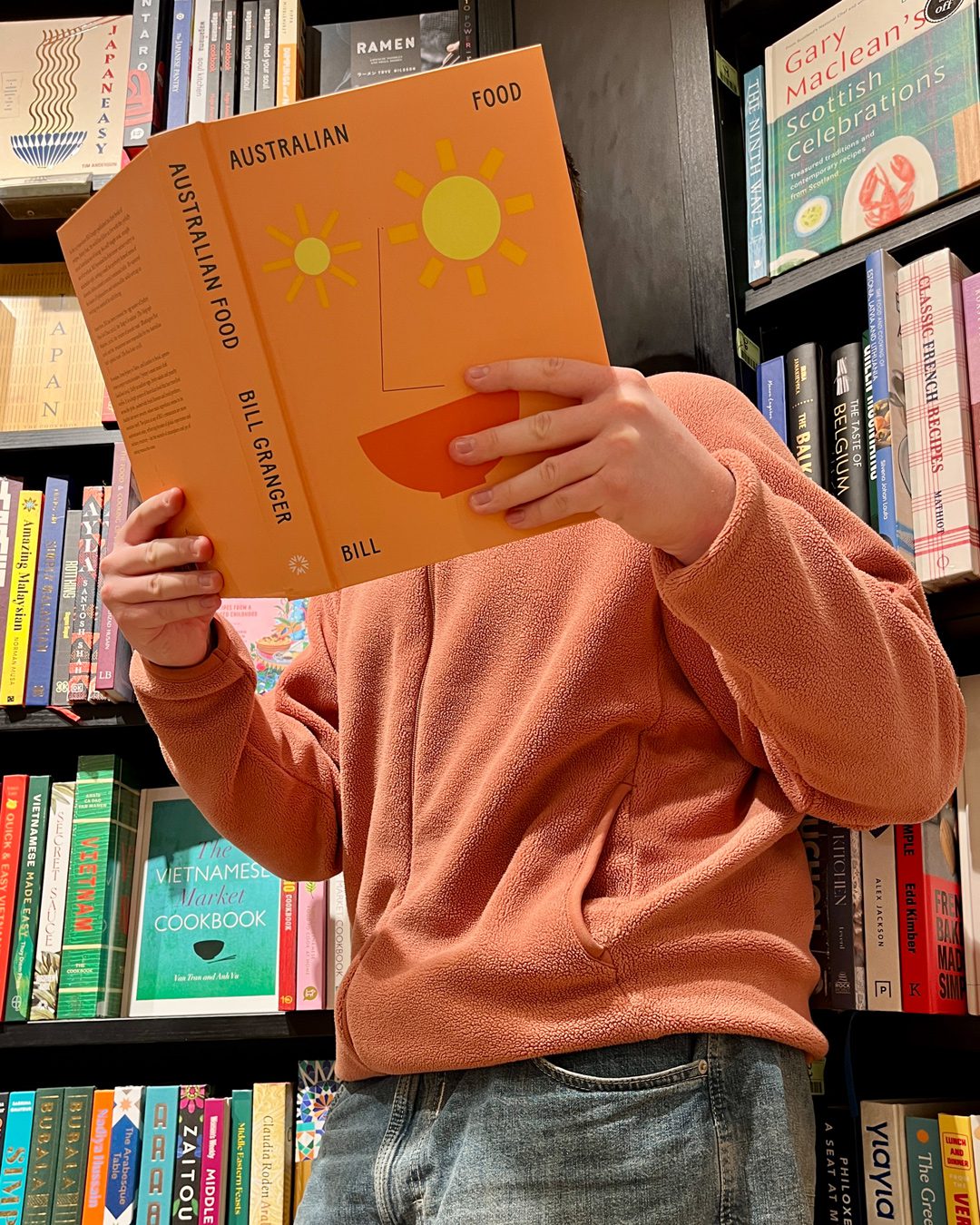 Figure in orange jacket reading a book in a bookstore with an orange face on the cover. Portraits for shy people