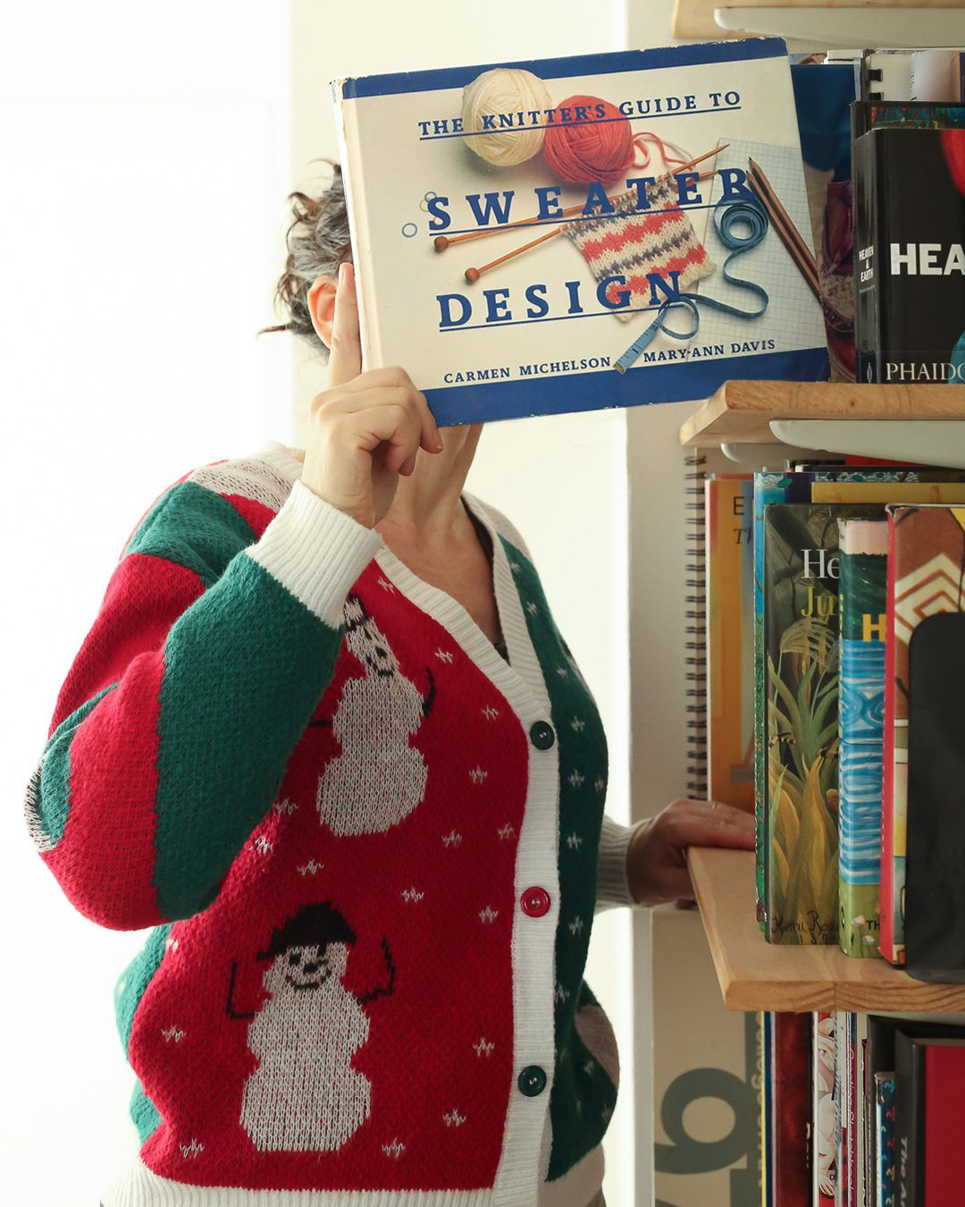 Woman in a christmas jumper pulling a book on sweater design out of the bookcase. Portraits for shy people