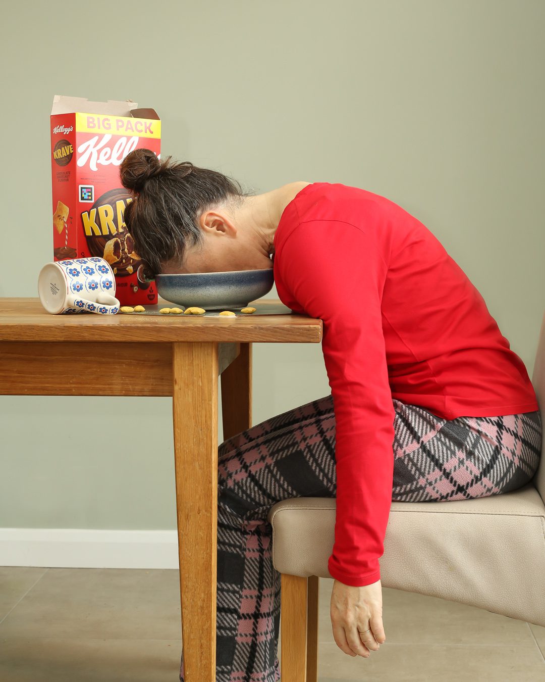 Woman in pyjamas sitting at breakfast table with her had ina breakfast bowl. Portraits for shy people