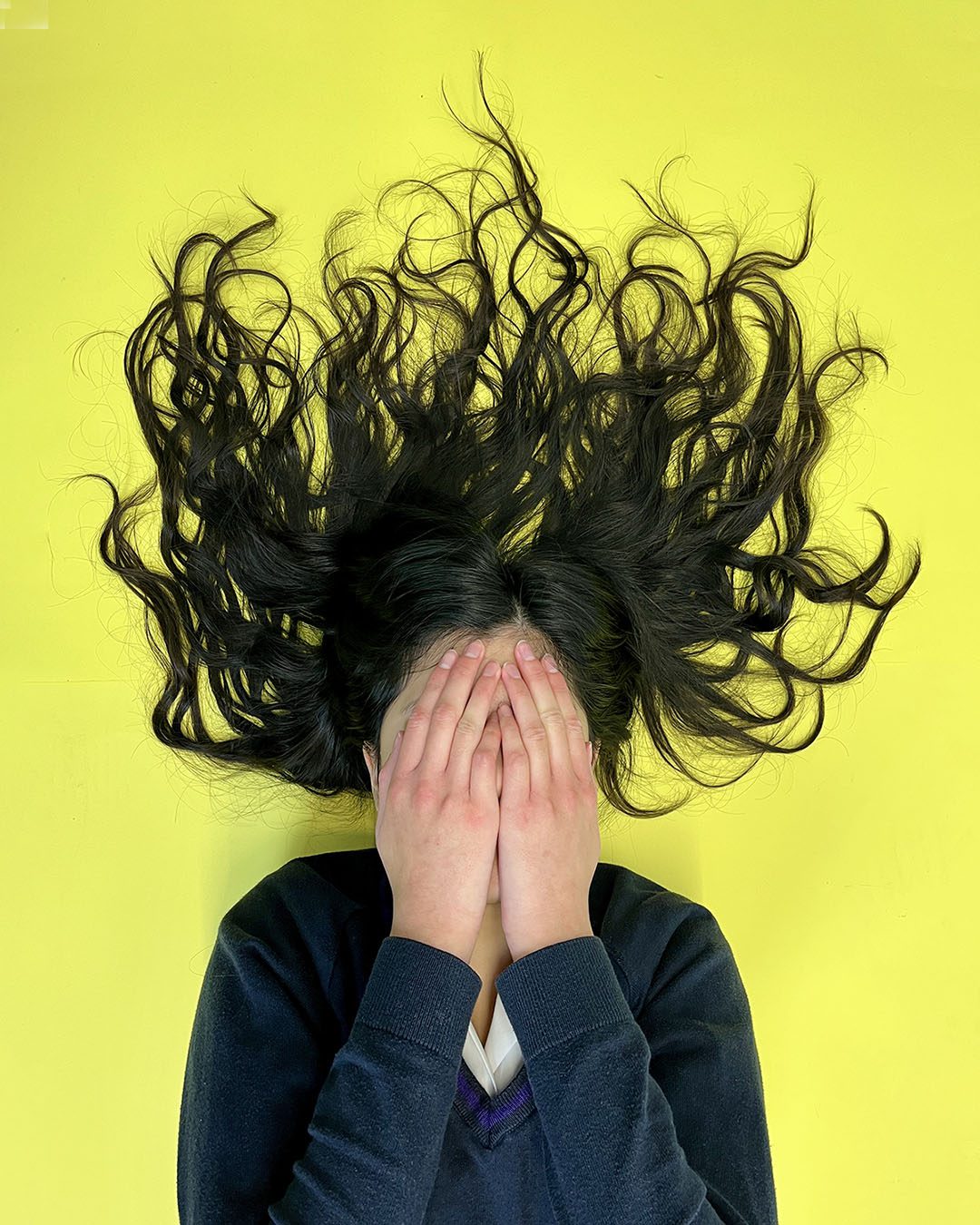Portrait of girl with hair spread around her on yellow background. hands over her face. Portraits for shy people
